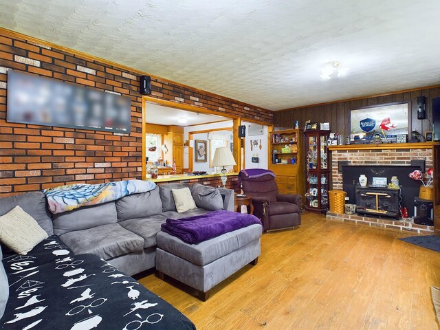 living room featuring brick wall, wooden walls, wood-type flooring, a fireplace, and a textured ceiling