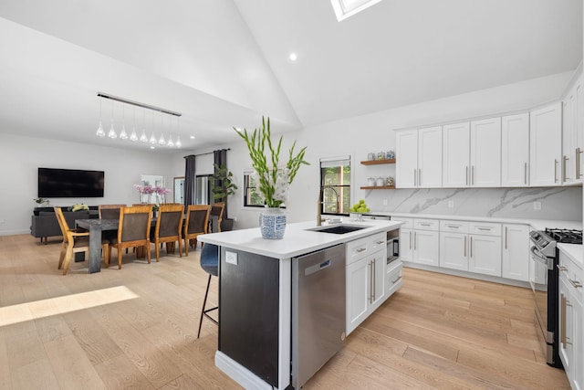 kitchen featuring tasteful backsplash, an island with sink, light hardwood / wood-style floors, stainless steel appliances, and white cabinetry