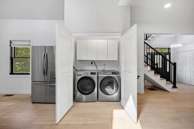 laundry room featuring light hardwood / wood-style flooring, cabinets, an inviting chandelier, and independent washer and dryer