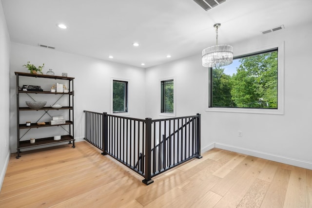 corridor with a wealth of natural light, light hardwood / wood-style flooring, and a chandelier