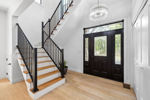 foyer with a towering ceiling, light hardwood / wood-style flooring, and an inviting chandelier