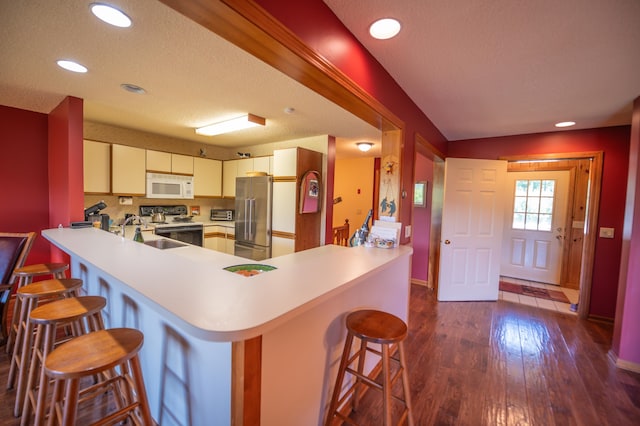 kitchen with a breakfast bar, stainless steel appliances, sink, kitchen peninsula, and dark wood-type flooring