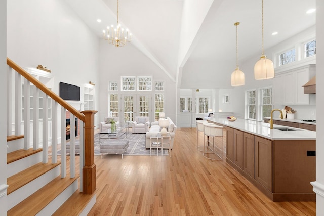 kitchen featuring pendant lighting, a kitchen island with sink, light hardwood / wood-style floors, sink, and high vaulted ceiling