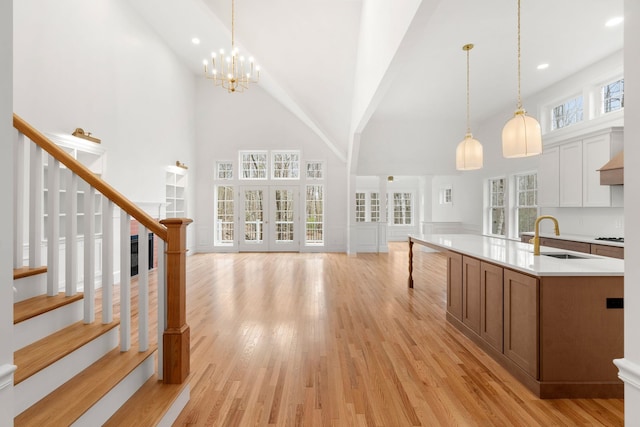 kitchen featuring decorative light fixtures, high vaulted ceiling, sink, and light hardwood / wood-style flooring