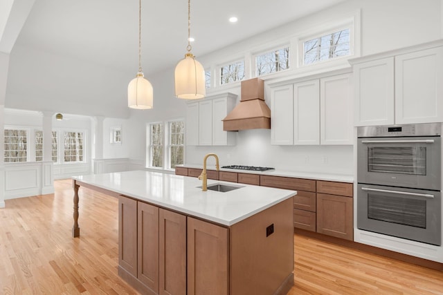 kitchen with light wood-type flooring, custom exhaust hood, white cabinetry, sink, and double oven