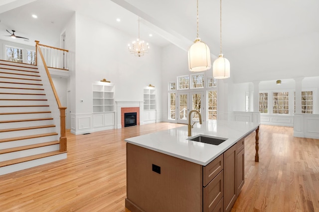 kitchen featuring a brick fireplace, light wood-type flooring, sink, an island with sink, and high vaulted ceiling