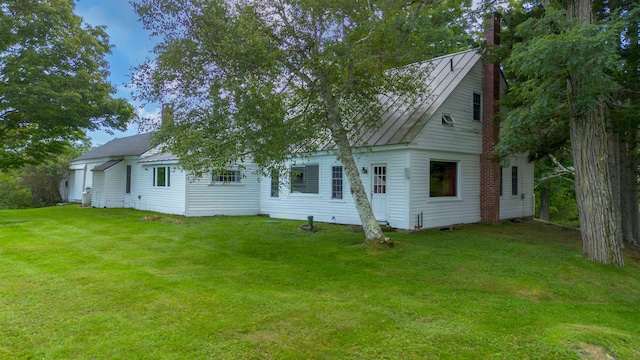 rear view of house featuring a standing seam roof, a lawn, a chimney, and metal roof