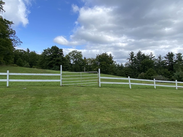 view of gate with a rural view, a lawn, and fence