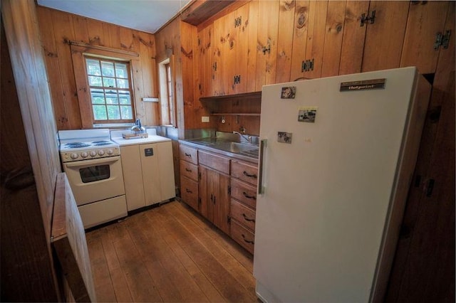 kitchen with white appliances, wooden walls, hardwood / wood-style flooring, light countertops, and a sink