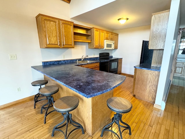 kitchen with brown cabinetry, dark countertops, a peninsula, black appliances, and a kitchen bar