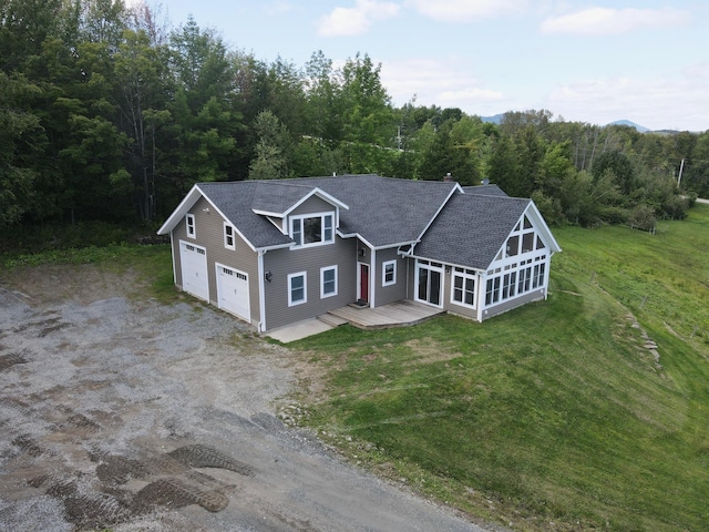 view of front facade featuring a garage, a sunroom, driveway, a wooden deck, and a view of trees