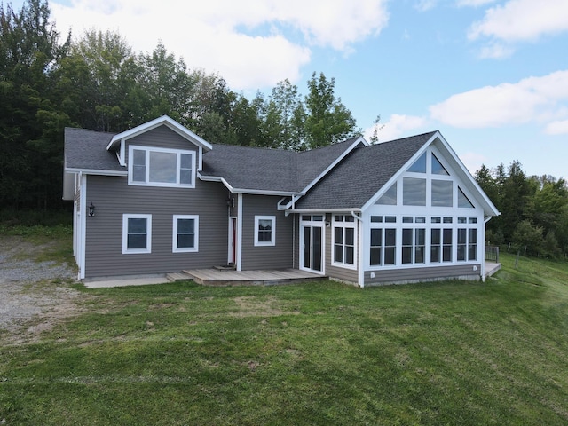 back of property featuring a sunroom, a deck, a lawn, and roof with shingles