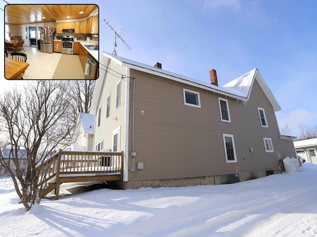 view of snowy exterior featuring a chimney and a wooden deck