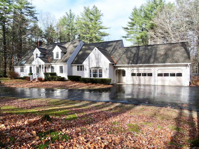 cape cod home featuring aphalt driveway, a chimney, and an attached garage