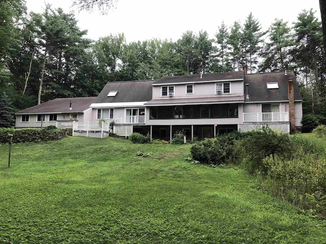 back of property with a lawn, a chimney, a sunroom, and a wooden deck