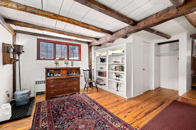 interior space with radiator, light wood-style floors, beam ceiling, and wooden walls