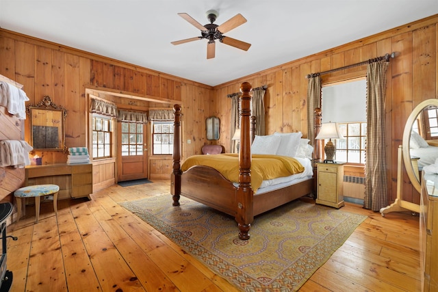 bedroom featuring a ceiling fan, ornamental molding, hardwood / wood-style floors, and wooden walls