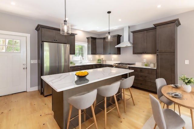 kitchen with stainless steel appliances, a sink, dark brown cabinets, a center island, and wall chimney exhaust hood