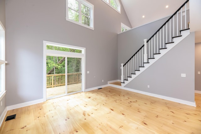 unfurnished living room with visible vents, stairway, a high ceiling, wood finished floors, and baseboards