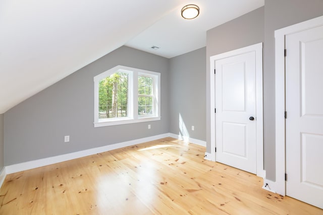 additional living space featuring light wood finished floors, baseboards, visible vents, and vaulted ceiling