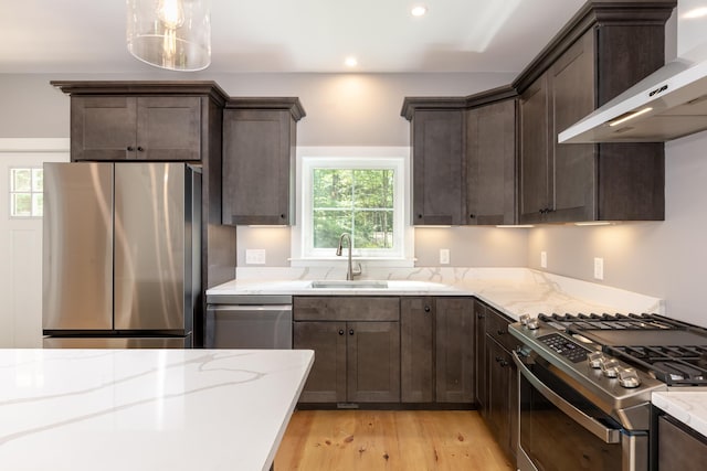 kitchen featuring stainless steel appliances, wall chimney range hood, a sink, and dark brown cabinetry