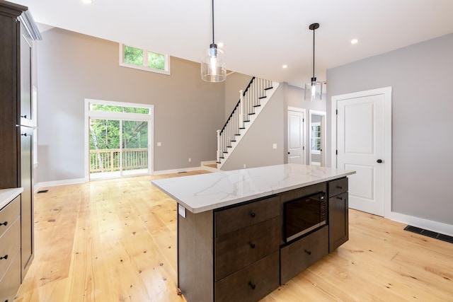 kitchen with hanging light fixtures, light wood finished floors, dark brown cabinetry, and built in microwave