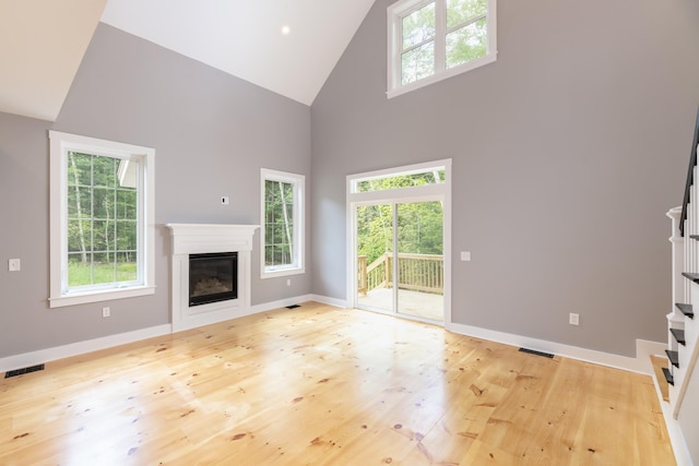 unfurnished living room with wood finished floors, visible vents, a healthy amount of sunlight, stairs, and a glass covered fireplace