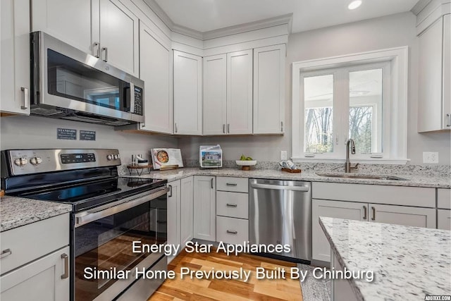 kitchen with appliances with stainless steel finishes, light stone counters, sink, light hardwood / wood-style floors, and white cabinetry