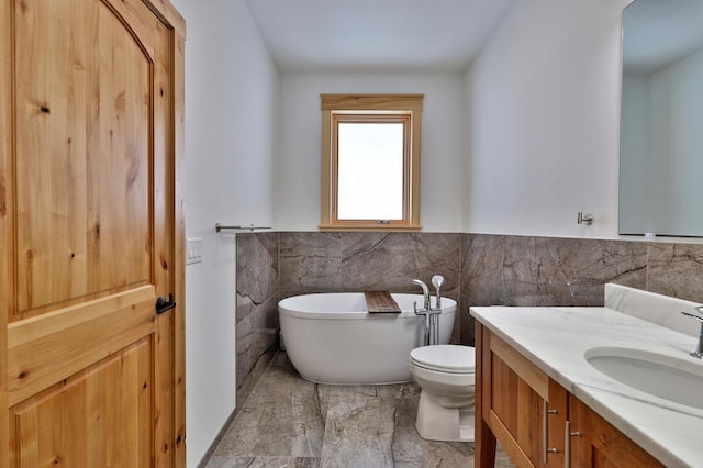 bathroom with tile walls, a soaking tub, toilet, wainscoting, and vanity