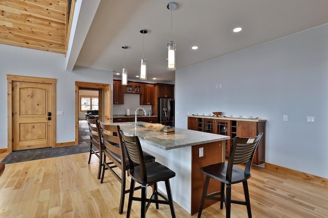 kitchen with light wood-type flooring, a breakfast bar, baseboards, and stainless steel fridge with ice dispenser