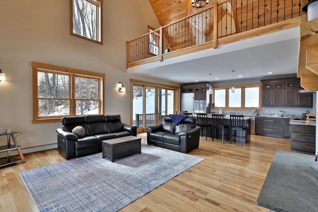 living room featuring a baseboard heating unit, a wealth of natural light, light wood-style flooring, and a high ceiling