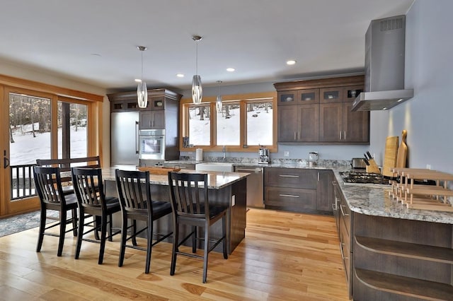 kitchen with a breakfast bar area, dark brown cabinetry, island range hood, stainless steel appliances, and light wood-style floors