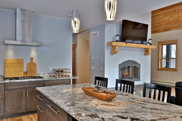 kitchen featuring light stone counters, stainless steel gas cooktop, visible vents, a glass covered fireplace, and wall chimney exhaust hood