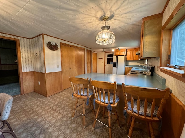 kitchen with a notable chandelier, wooden walls, kitchen peninsula, sink, and refrigerator with ice dispenser