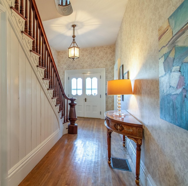 entrance foyer featuring wallpapered walls, baseboards, visible vents, stairway, and hardwood / wood-style floors