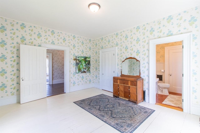 interior space featuring connected bathroom, wood finished floors, baseboards, a closet, and wallpapered walls