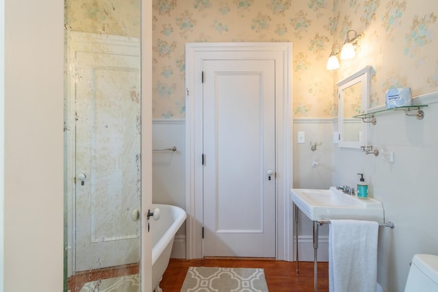 full bath featuring a soaking tub, wainscoting, wood finished floors, and wallpapered walls