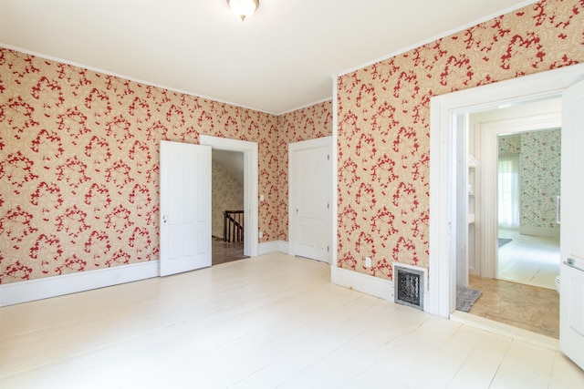 spare room featuring wallpapered walls, baseboards, visible vents, and wood finished floors