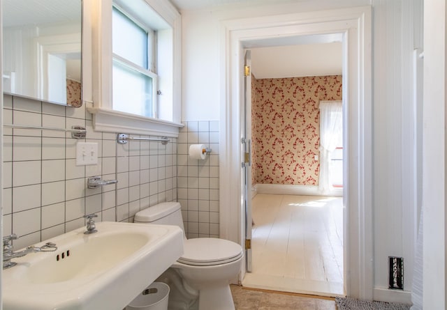 bathroom featuring a sink, tile walls, toilet, and wallpapered walls