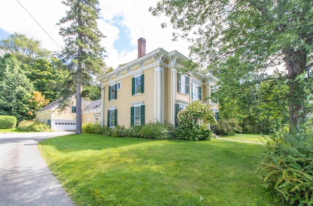 view of side of home featuring a chimney, a detached garage, and a yard