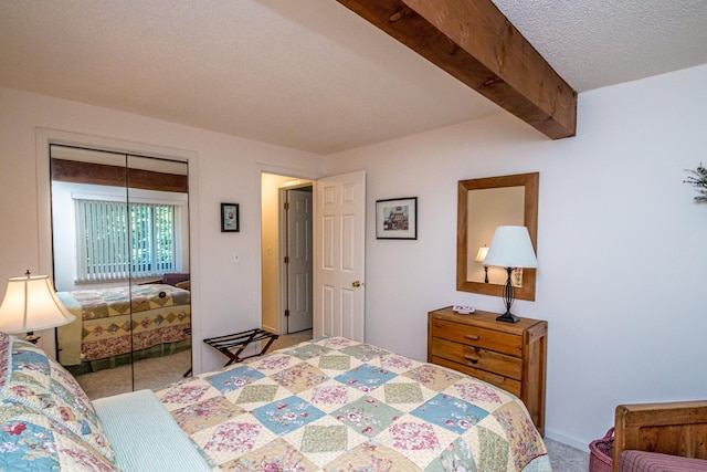 carpeted bedroom featuring a textured ceiling, a closet, and beam ceiling