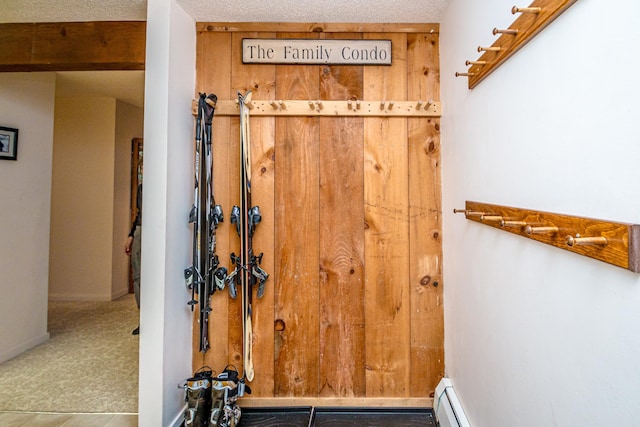 interior space featuring carpet, wooden walls, baseboard heating, and a textured ceiling