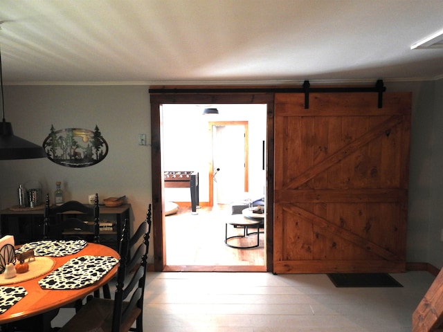 dining area with a barn door, crown molding, and light hardwood / wood-style flooring