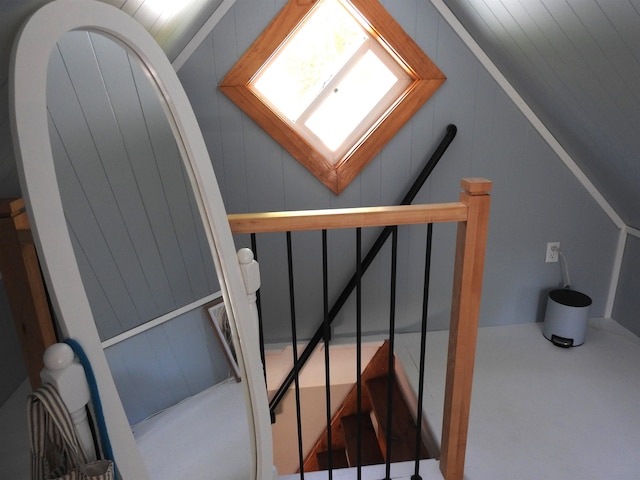 staircase featuring lofted ceiling and wood walls