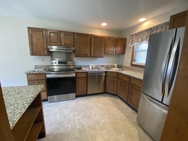 kitchen featuring recessed lighting, appliances with stainless steel finishes, a sink, light stone countertops, and under cabinet range hood