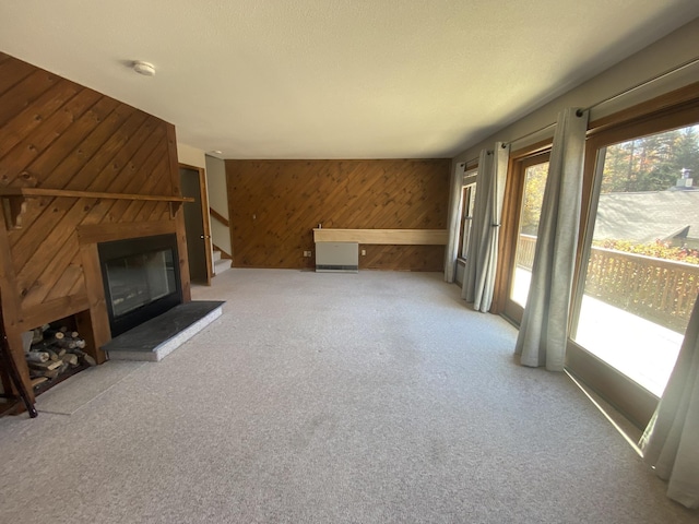 unfurnished living room featuring a large fireplace, stairs, wooden walls, and carpet flooring