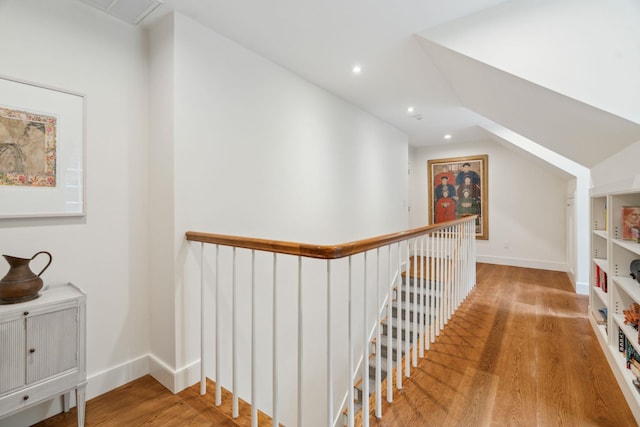 corridor with built in features, vaulted ceiling, and hardwood / wood-style flooring