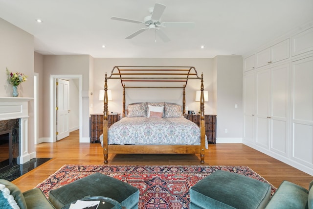 bedroom with a high end fireplace, light wood-type flooring, a closet, and ceiling fan