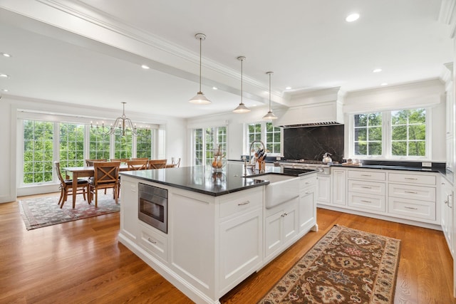 kitchen featuring built in microwave, crown molding, an island with sink, decorative light fixtures, and white cabinets