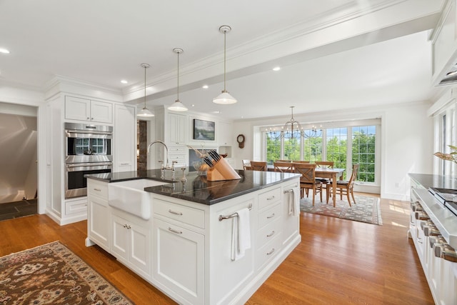 kitchen featuring a kitchen island with sink, white cabinets, sink, hanging light fixtures, and stainless steel double oven